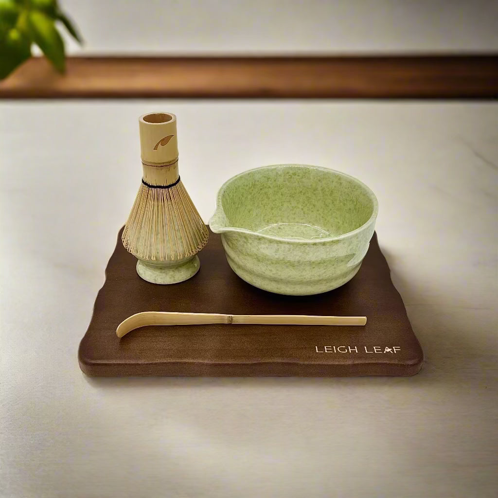 Discover the beauty of the 5 Piece Matcha Whisk Set with Wooden Display Board from Leigh Leaf, showcasing a green matcha bowl, bamboo whisk, and a wooden base for a refined tea experience.