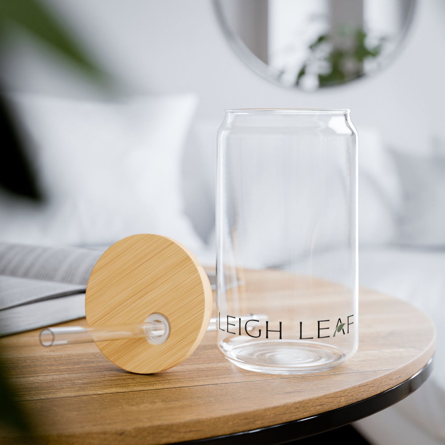 The Leigh Leaf Elegant 16oz Matcha Sipper Glass next to its bamboo lid and straw on a coffee table, perfect for matcha glass sipper enjoyment in a cozy setting.
