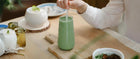 A person stirring a refreshing glass of matcha while enjoying breakfast, highlighting the benefits of drinking matcha in the morning for energy and wellness.